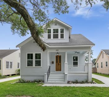 A newly constructed home by Viridis Construction, featuring a classic white exterior with a welcoming front porch, a wooden front door, and meticulous landscaping. The design combines modern touches with timeless charm on a well-kept grassy lot.