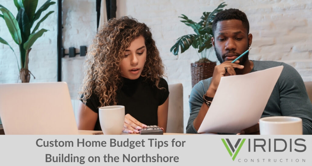 A couple reviewing documents and using a calculator while planning a custom home budget, with a laptop and coffee on the table. Highlights the importance of budgeting for building a custom home on the Northshore, guided by Viridis Construction’s expertise.