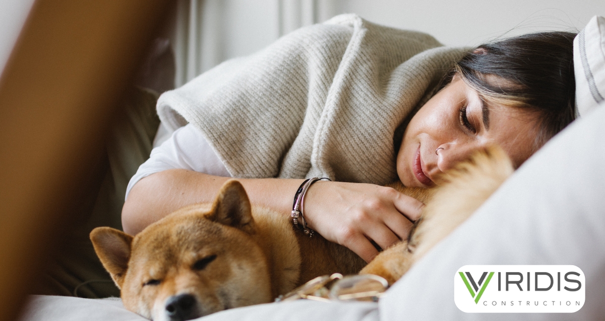 A woman snuggled up with her dog on a cozy bed, wrapped in a warm blanket. Highlights the comfort and warmth of a well-prepared home for winter, emphasizing Viridis Construction's focus on creating safe and inviting spaces.